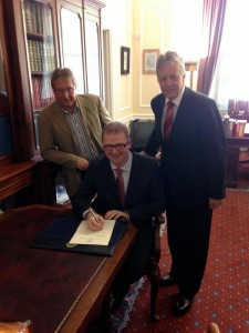 Simon Hamilton signs in as the new Stormont Finance Minister watched by First Minister Peter Robinson and outgoing minister Sammy Wilson