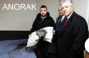 John Smyth jnr holds up scorched pillow as his father and DUP leader Peter Robinson look on
