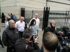 Willie Frazer with Jamie Bryson behind him in flowing locks and with tape over his mouth