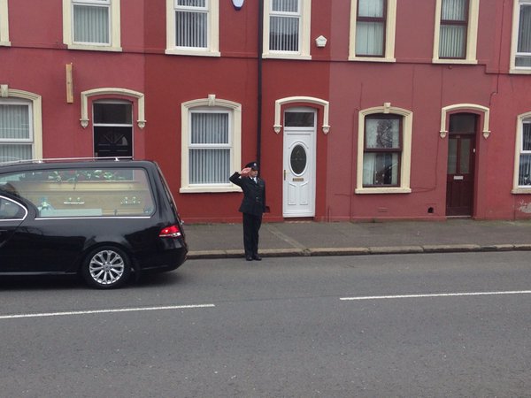 A police officer salutes the coffin of prison officer Adrian Ismay in east Belfast today
